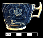Pearlware London shape handled cup reverse printed underglaze in dark blue. Field dots decorative device forms background behind flowers.  4” rim diameter, 2.5” vessel height.